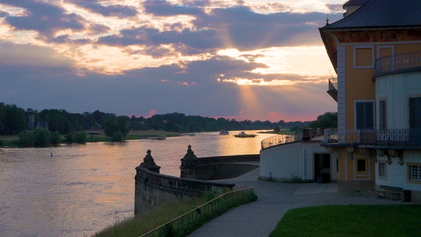 Orange sunset on river.River idyllic landscape at sunset. ferry transports people from one side to other. In foreground is a small palace. Slow motion. Elbe River. Dresden, Pillnitz, Germany
