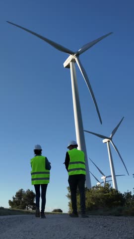 Two engineers, man and woman, with a digital tablet, inspect wind turbines and electricity generators. Clean energy, sustainability, and renewable energy maintenance.