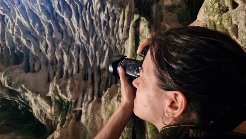 Brunette curious woman taking pictures with camera inside a cave. Slow motion