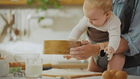 Kitchenware. Housewife cook using kitchen utensils happily sifts flour with child in modern kitchen. General camera view of Asian woman funny cooking using fashionable sling for support, baby - Powered by Shutterstock - Get 15% off with code: PIKWIZARD15