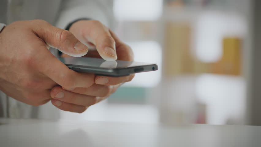 In a pharmacy, a European health worker holds a smartphone in his hands, using his skills and experience. In slow motion, he uses a touch phone to operate, strictly following the rules of service