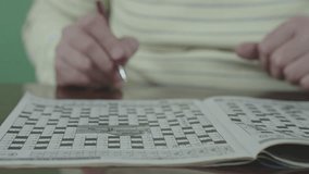 Elderly hands holding red pen solve crossword puzzle on white book. Old person is wearing yellow striped sweater. - Powered by Shutterstock - Get 15% off with code: PIKWIZARD15