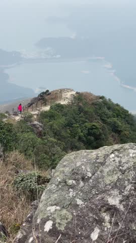A traveler walks along a narrow ridge overlooking the sea and the city