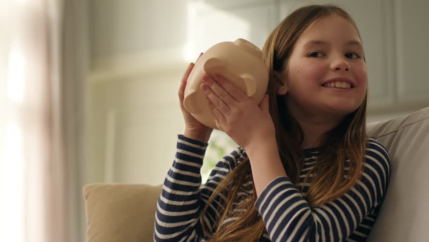 Happy little girl putting coins pennies pig piggy bank shaking finances save money dream child enjoy currency investment economy wealth planning kid female daughter budget cash security smile business