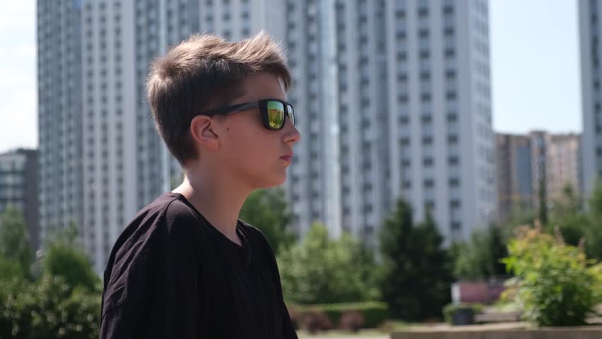 Portrait of teen school boy with his electro scooter. at a city park. Guy wearing sunglasses on summer holiday