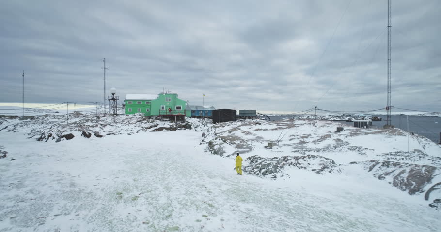 Man running polar research station on Antarctica coastline, Vernadsky science base. Green house buildings on rocky ocean coast. Antarctic expeditions and travel. South Pole exploration. Drone flight