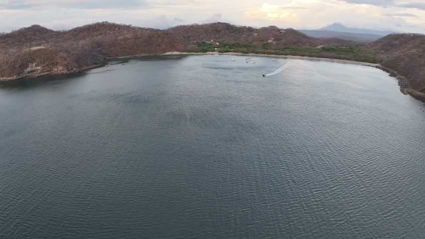 A drone view over El Jobo Bay with the beach and a motorboat sailing on the ocean at sunset in Costa Rica, Guanacaste, central America