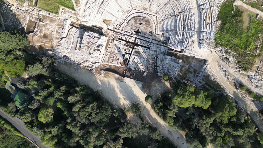 Overhead drone flight over ruins of ancient Greek theatre (Teatro Greco) in archaeological park in Syracuse, historic landmark and tourism in Sicily Italy
