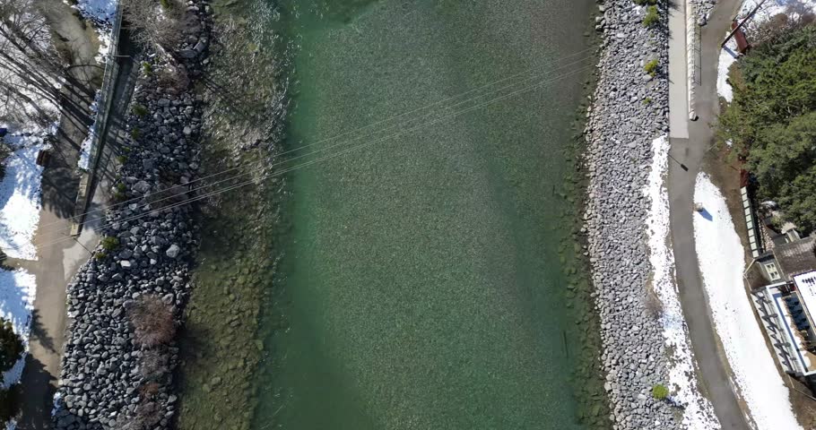 An aerial view of cars driving on river bridge surrounded by snowy forests, and mountain seen in the background