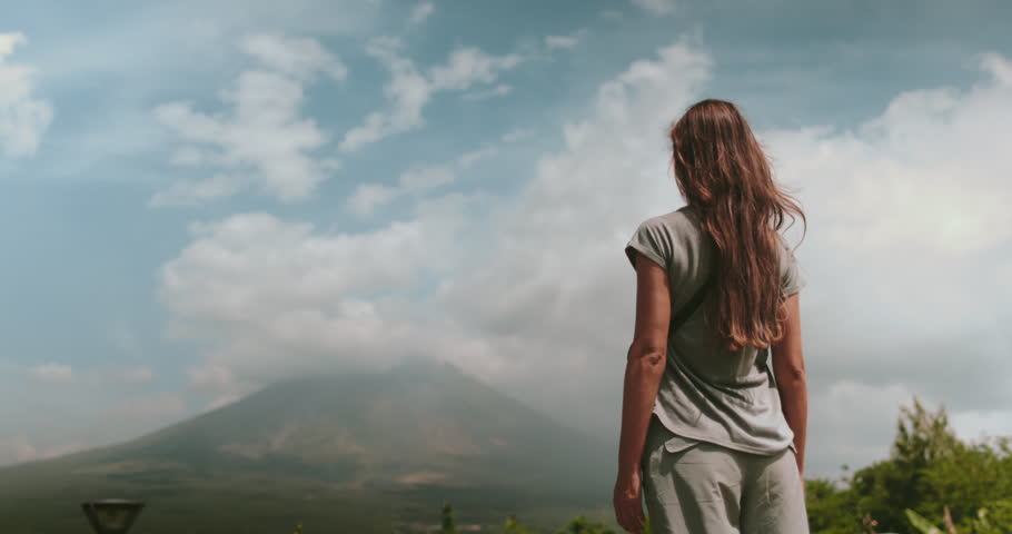 Woman enjoy Legazpi Mountains Volcano, Philippines. Asia wild nature tropical landscape. Tourist female rise hands slow motion, relax, outdoor lifestyle travel on summer holiday vacation. Back view