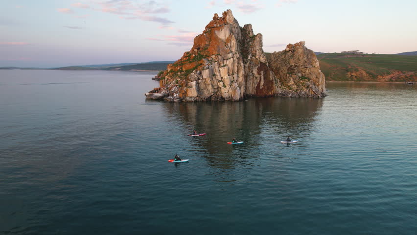 Sunset over Lake Baikal in summer. Tourists swim on sap boards in the bay of the lake. Active water recreation.