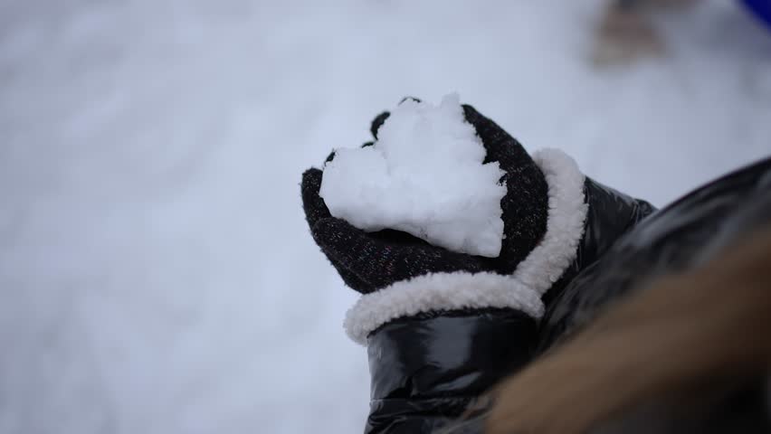 Gloved hand holds snow in shape of heart. Concept of winter entertainment.