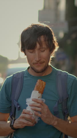 A delighted tourist savors the taste of Turkey, enjoying a freshly made balik ekmek wrap on the bustling streets of Istanbul. Vertical video.