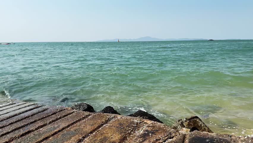 Coastal landscape with aquamarine waters lapping against a rocky shoreline and creating light splashes