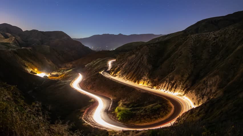 Night time lapse of a road winding through the mountains.