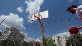 Lively young man actively engaging in shooting basketball towards hoop during outdoors game against backdrop of basketball court under cloudy blue sky. Concept of entertainment, hobby and leisure. - Powered by Shutterstock - Get 15% off with code: PIKWIZARD15
