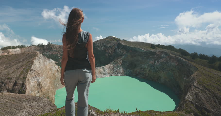 A woman stands confidently on the summit of a mountain overlooking a pristine lake formed within a volcanic crater. The breathtaking view showcases the unique beauty of the Philippine landscape.