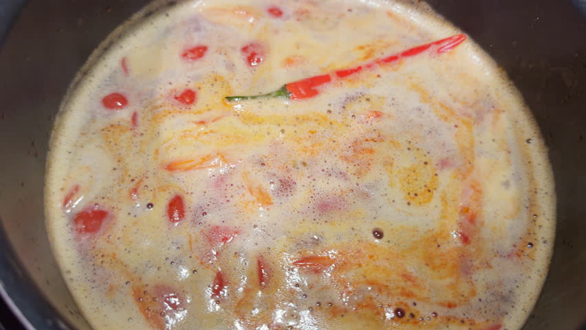 Cooking a traditional Asian dish tom yam soup, boiling liquid with tomatoes and red pepper