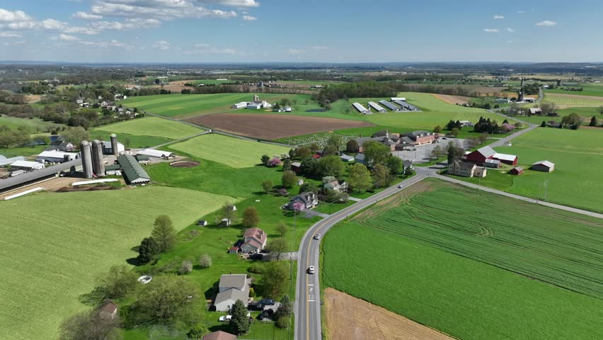 Bright green farmland in spring season. Traffic on rural road surrounded by farm fields. Aerial truck shot of rural USA farming community. Backward flight.