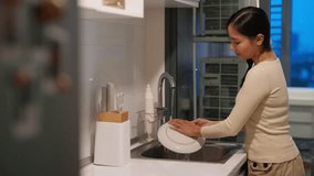 Happy Asian woman do housework washing dishes in the sink after dinner in the kitchen at apartment. Attractive girl using dishwashing liquid and sponge cleaning kitchenware at home kitchen in evening. - Powered by Shutterstock - Get 15% off with code: PIKWIZARD15