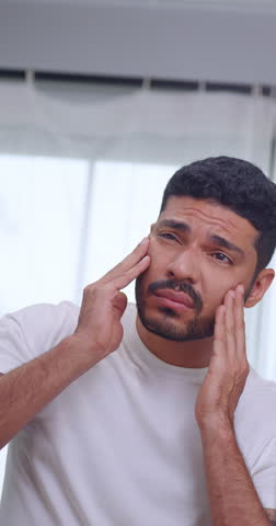 Vertical clip. A handsome young man is worried about the wrinkles on his face while looking in the mirror.