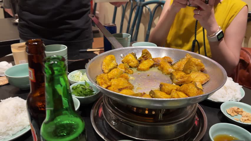 A professional chef using chopsticks to adds cilantro and spring onion to the traditional and popular dish of boneless grilled hemibagrus fish, known as Cha Ca Hanoi, a fried river catfish.