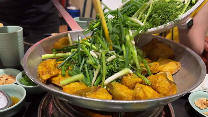 A professional chef using chopsticks to adds cilantro and spring onion to the traditional and popular dish of boneless grilled hemibagrus fish, known as Cha Ca Hanoi, a fried river catfish.