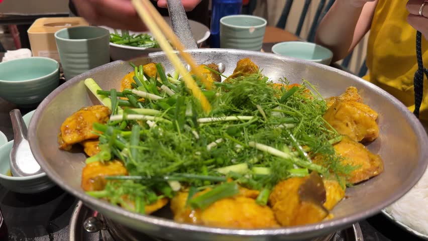 A dish of boneless grilled hemibagrus fish, a type of river catfish fried called Cha Ca La Vong Hanoi, table of diners with fresh dill and spring onion, eating with cilantro