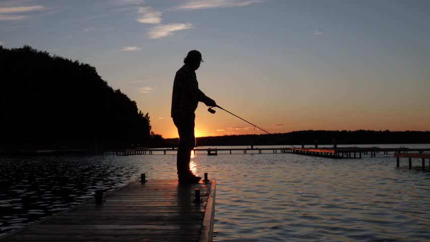 a man stands on a wooden dock at sunset in the evening fishing