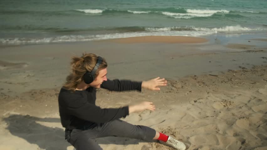 A drunk man dances intricately on the beach to music on headphones, gets a buzz while walking alone along the sandy seashore.