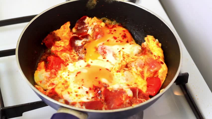 Sizzling frying pan with eggs frying. Eggs with pastirma cooking on stove. 
