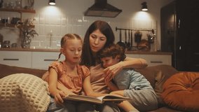 Girl sits on couch reading storybook to mother and younger brother. Evening scene with warm lighting. Concept of family bonding and education. Focus on reading, storytelling, and togetherness - Powered by Shutterstock - Get 15% off with code: PIKWIZARD15
