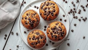 Delicious, homemade chocolate chip muffins on a white plate, surrounded by scattered chocolate chips on a rustic wooden table. - Powered by Shutterstock - Get 15% off with code: PIKWIZARD15