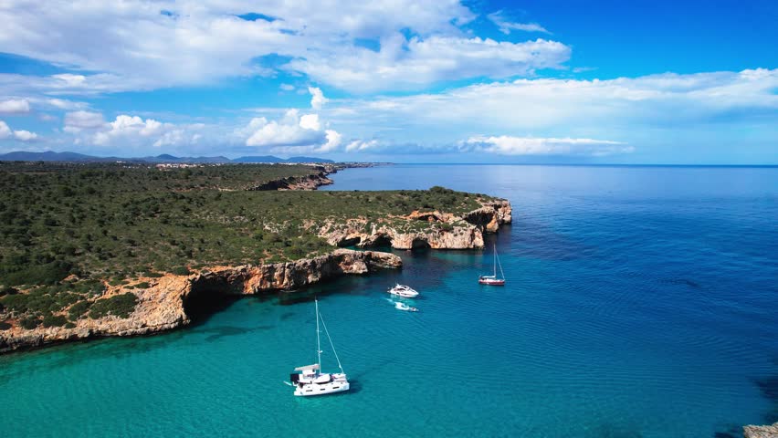 4K Aerial Drone video of the most incredible turquoise blue water color with a unique rocky cliff formation and boats anchored in on a beautiful summer sunny day, Cala Varques secluded beach, Mallorca