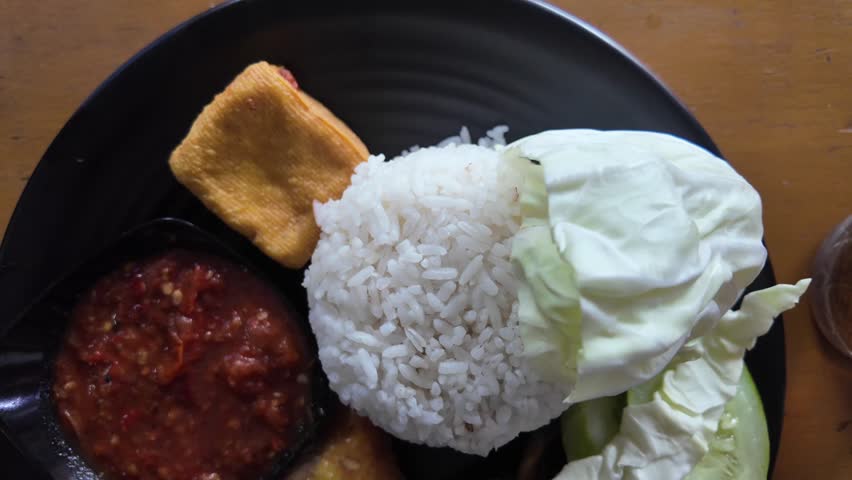 Indonesian food is called lalapan, there is white rice, fried chicken, tofu, tomato sauce, which is rotated to look a bit more cinematic