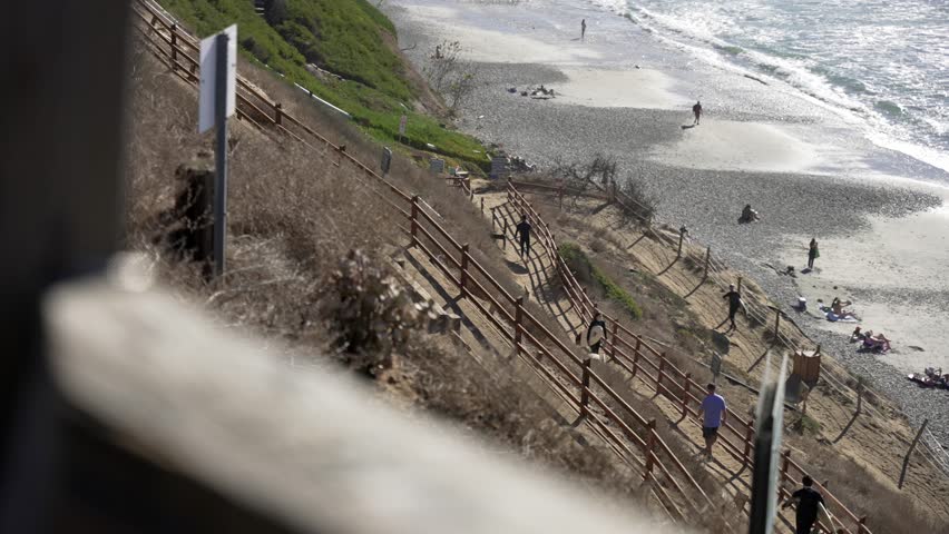 Surfers walking pathway to Leucadia beach surfing spot on a sunny day in San Diego California with waves crashing on the rocky shore