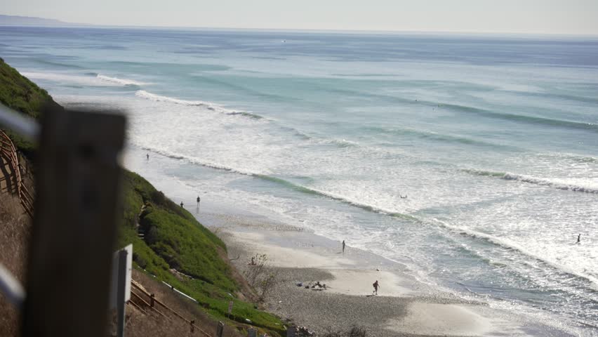 Surfers walking pathway to Leucadia beach surfing spot on a sunny day in San Diego California with waves crashing on the rocky shore