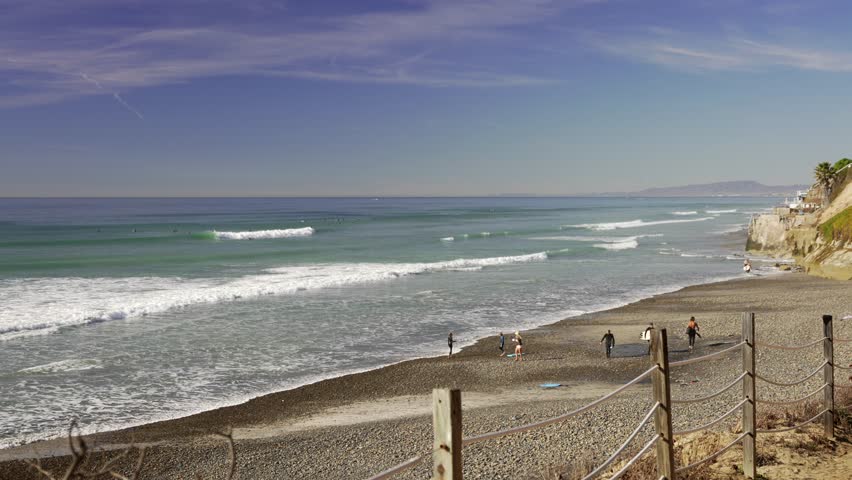 Surfers walking pathway to Leucadia beach surfing spot on a sunny day in San Diego California with waves crashing on the rocky shore