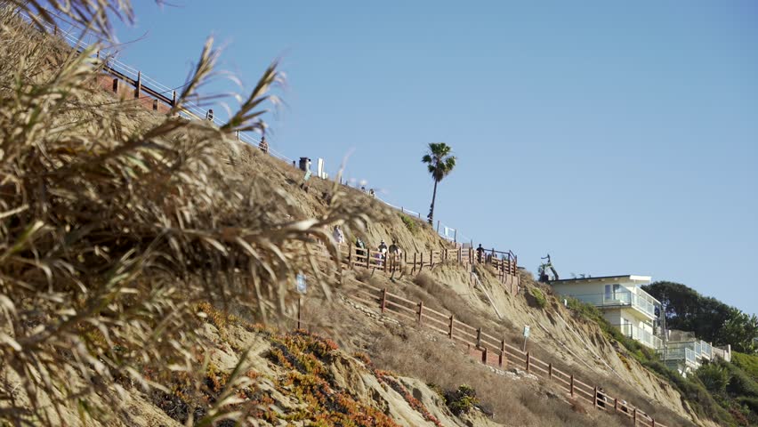 Surfers walking pathway to Leucadia beach surfing spot on a sunny day in San Diego California with waves crashing on the rocky shore
