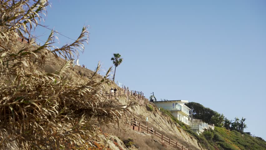 Surfers walking pathway to Leucadia beach surfing spot on a sunny day in San Diego California with waves crashing on the rocky shore
