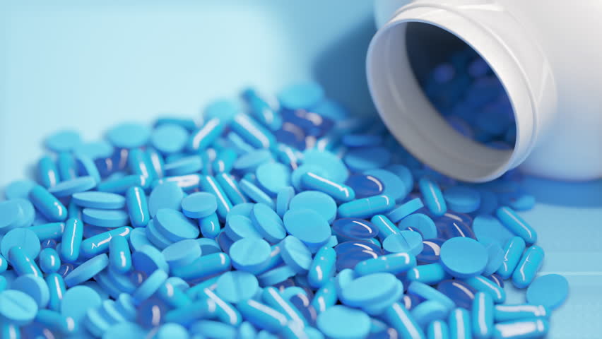 Close-up of a spilled bottle with various blue pills and capsules, representing pharmaceutical medication and healthcare.