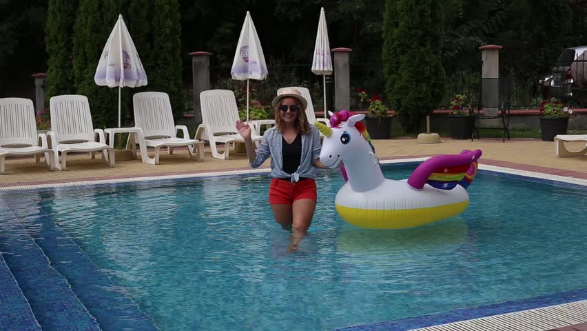 Woman in swimsuit sitting on inflatable unicorn pool float in pool in the hotel. Summer holidays
