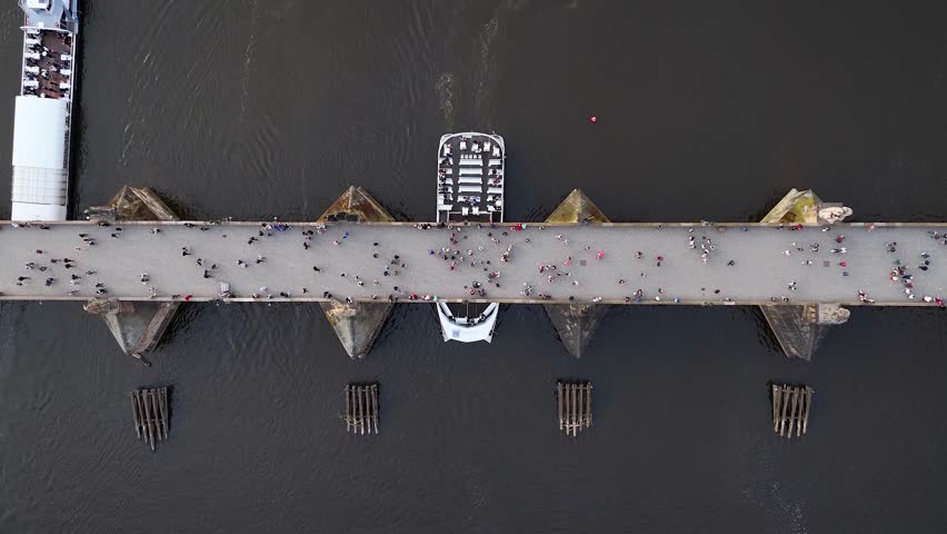 Aerial top down view of the Charles Bridge in Prague, Czech Reublic, with people walking and boats on sightseeing tour