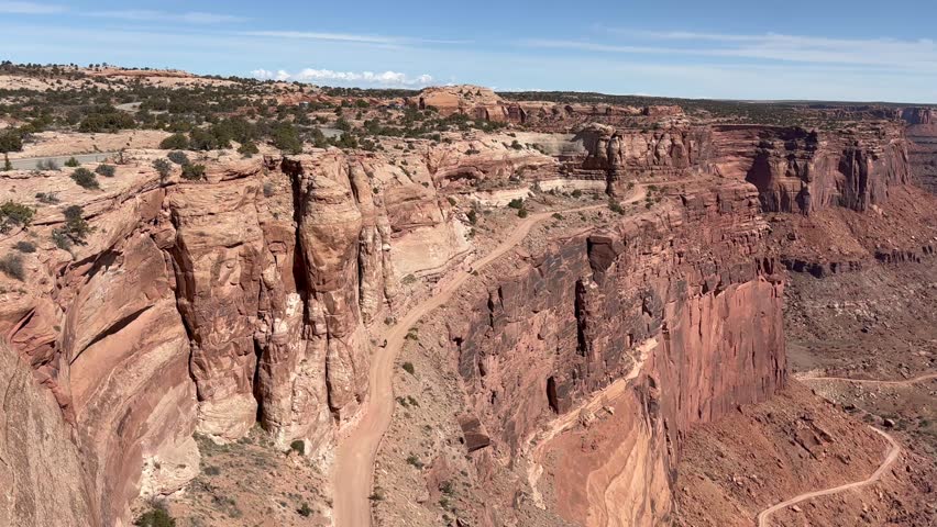 Stunning aerial perspective of Canyonlands National Park as motorcycles navigate the iconic Shafer Trail Road switchbacks. The adventurous pair ride the narrow and steep cliff road - Utah, USA
