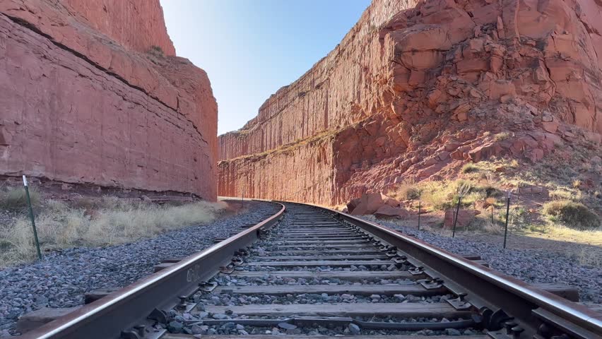 Static shot of an empty railway track cuts through a red rock canyon near Moab, Utah, USA. The shot gives a sense of adventure, travel, and the vastness of nature. Taken on the Corona Arch trail.
