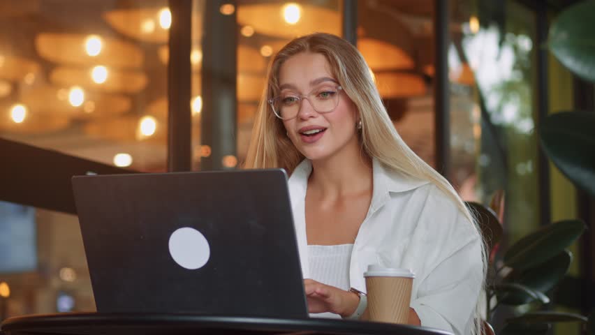 Picturesque cafe with green plants smiling freelancer woman immersed in work on laptop remote work. Stunning cafeteria with green plants blonde happy freelancer woman working on computer remote work.