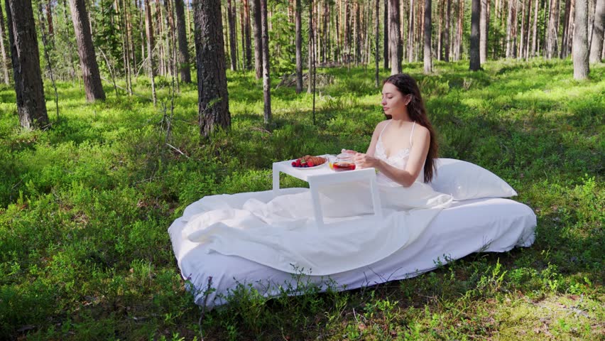Woman wakes up in a summer forest. Young woman has breakfast in bed in a summer forest