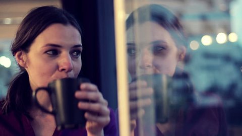 Sad, depressed woman drinking tea by the window in home

