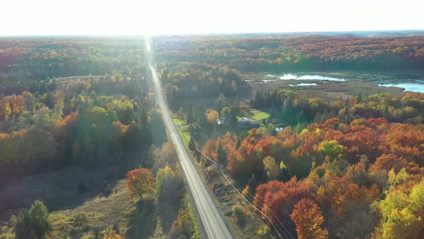 An aerial drone shot moving over a road, marsh, forest and towards a lake at sunset during autumn