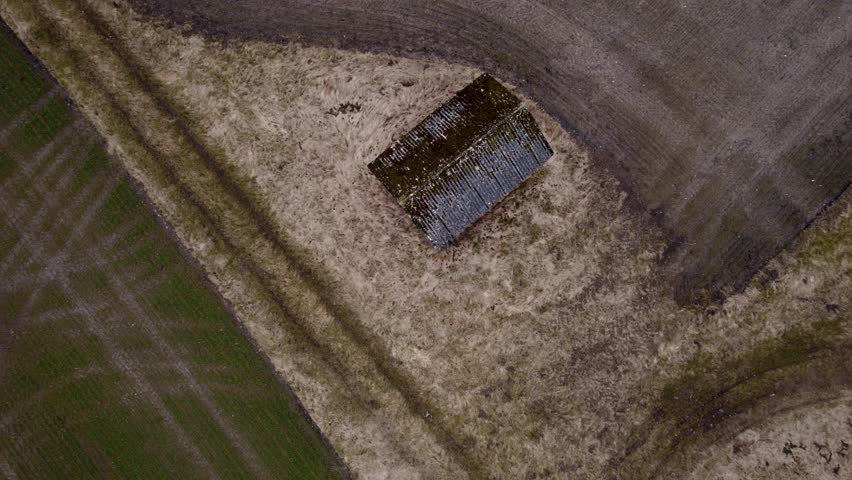 A wooden shack on the countryside, surrounded by brown fields.